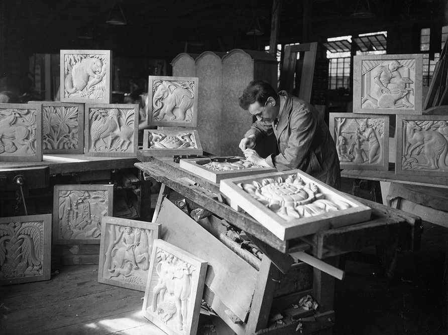 Denis Dunlop working in his studio on the panels of a screen representing the fauna, industries, people and flora of the five Dominions, to be installed in the Henry Florence Memorial Hall of the Royal Institute of British Architects, 66 Portland Place, London.