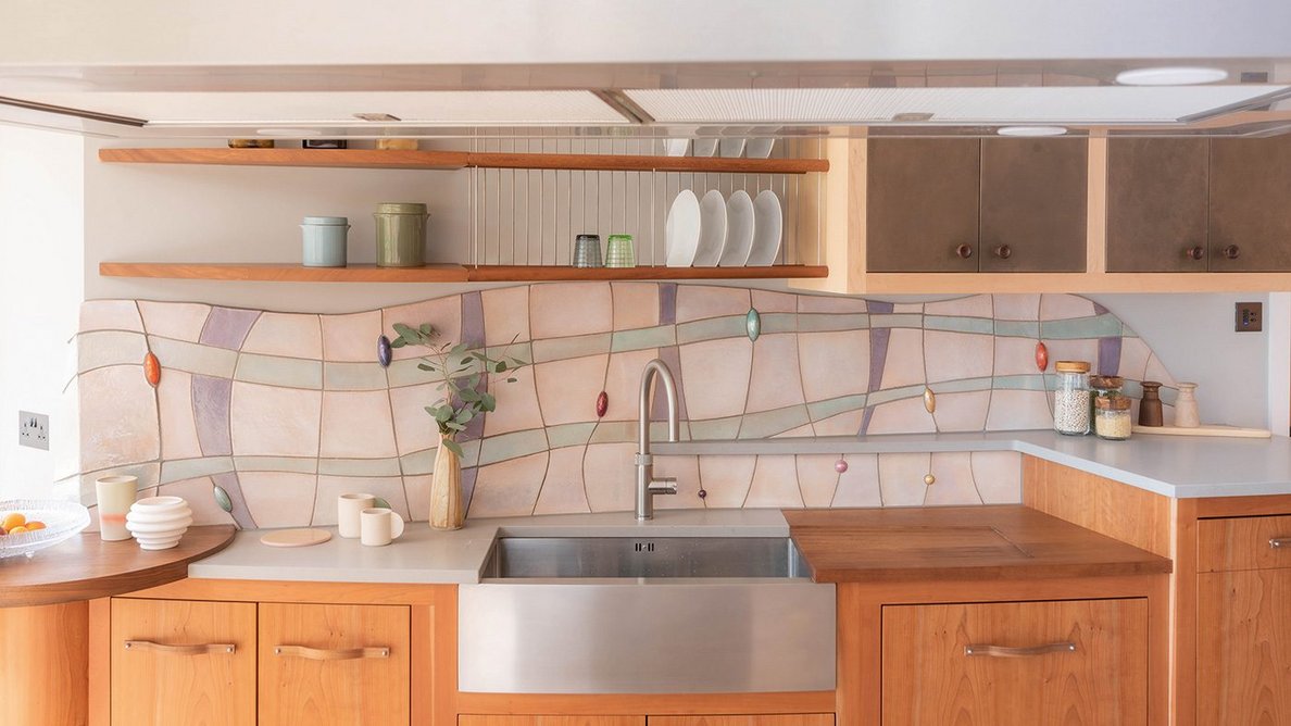 Artisan tiling by Alex Zdankowicz forms a sinuous design above kitchen units, including a dishwasher cabinet elevated for ease of use.