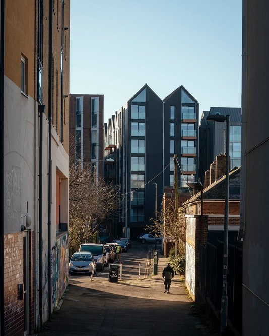 Private residential building viewed from the east. Blocks are planned to resemble rows of townhouses, each with twin bays, projecting balconies and gabled roofs.