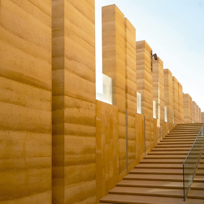 A castellated wall of rammed earth  screens a staircase  and external walkway.