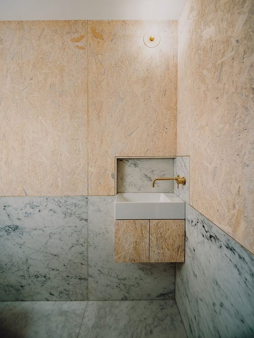 Brass-edged SterlingOSB Zero boards contrast with Carrara marble in the downstairs toilet.