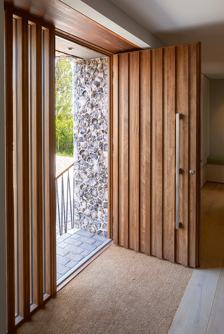 The richly coloured bespoke iroko wood front door is designed to contrast with the weathering sweet chestnut of the cladding.