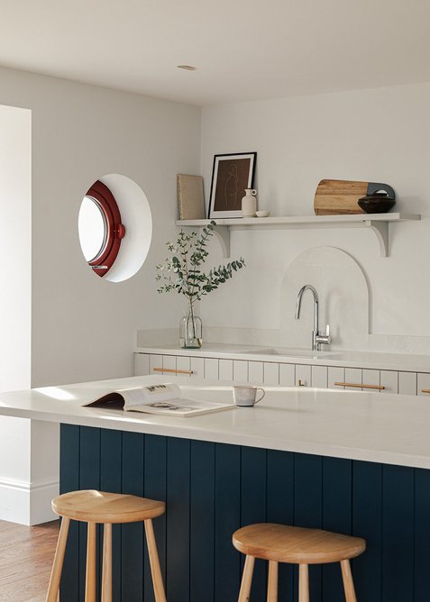 A porthole-style window playfully echoes the facade’s red tiles and steel.