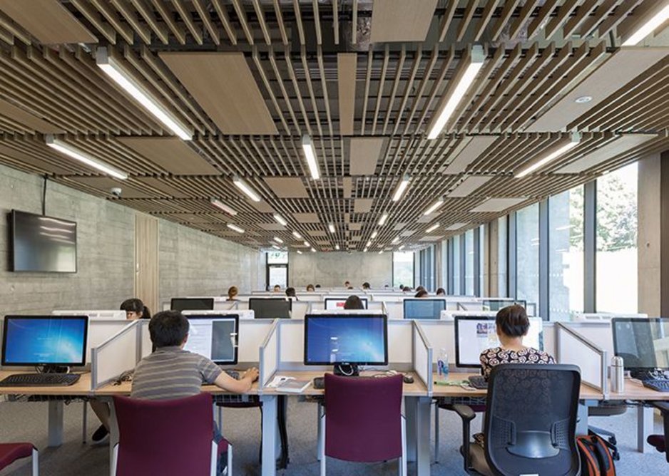 In the library extension's post-graduate study space, the necessary mechanical ventilation kit is masked in line with the attenuating oak slat detailing elsewhere.