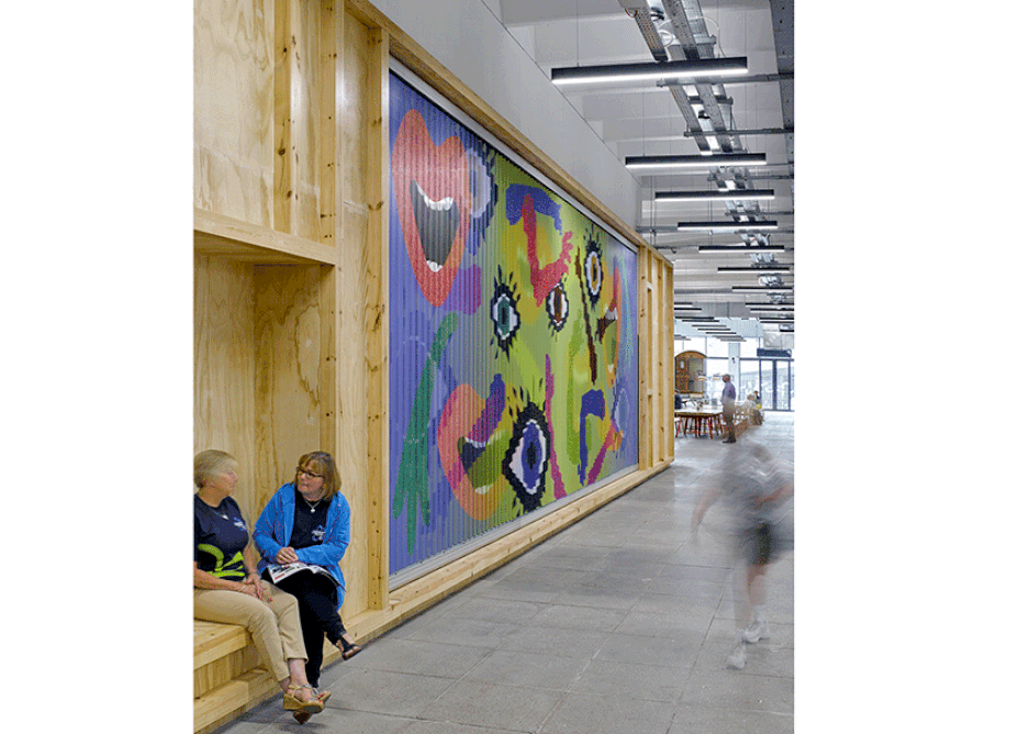 The ‘People’s Wall’ is a trivision billboard featuring work by artists with the community (or: integrated seating allows shoppers to ‘inhabit’ the wall)