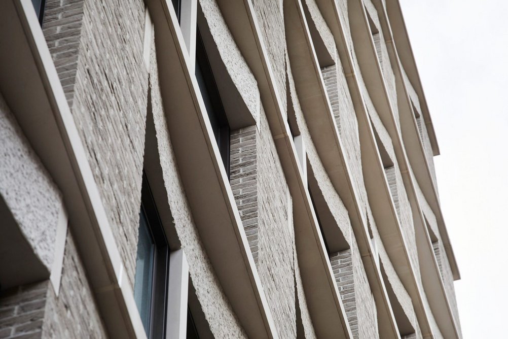 The facade combines brick  slip piers with GRC mullions and scalloped,  textures lintels.