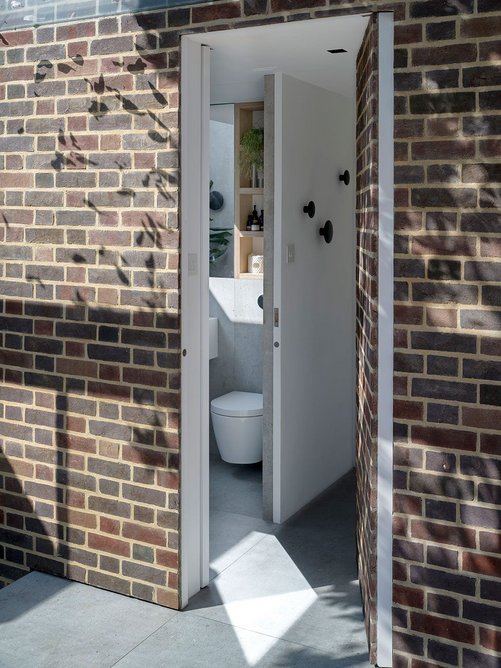The bathroom door is clad with brick to maintain the way the space mimics the external courtyard.