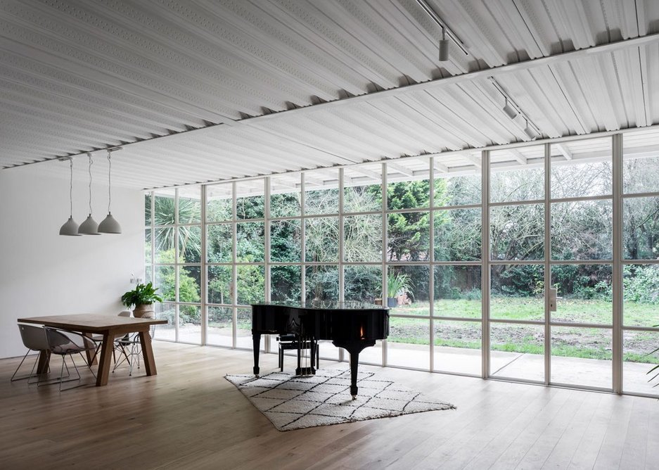 The column-free full width living/dining space exposes the steel-tray underside of the floor above: the steel-framed industrial glazing is thermally broken.