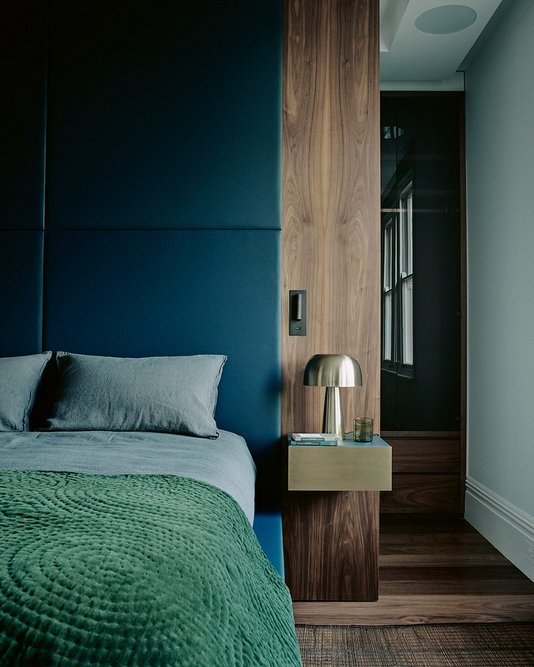 The master bedroom continues the palette of oak and luxurious dark blue leather on walls and storage. An opening leads to a narrow dressing room and marble bathroom beyond.