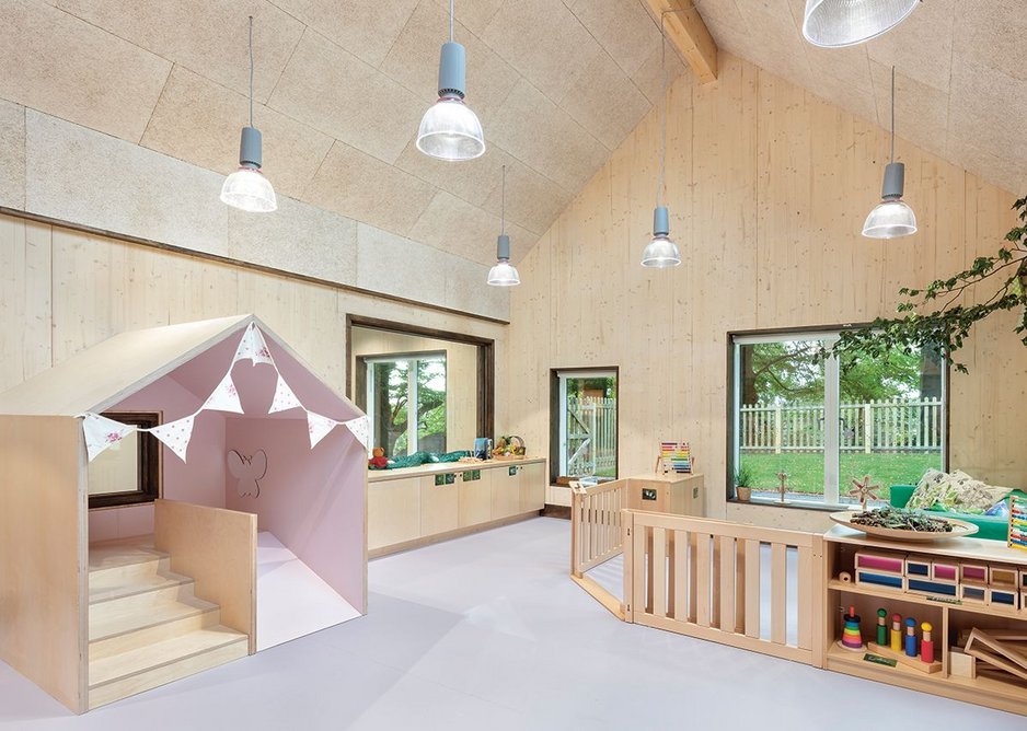 In the baby room, a small house with a short slide mimics the pitches of the classroom volume, which has exposed CLT panels and, on the ceilings, wood, fibre boards.