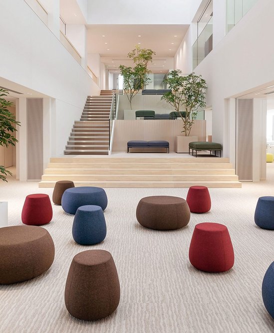 A gathering area fosters communication between adjacent lens and camera design departments. Furnished with Arper’s Pix ottomans and Steeve benches.