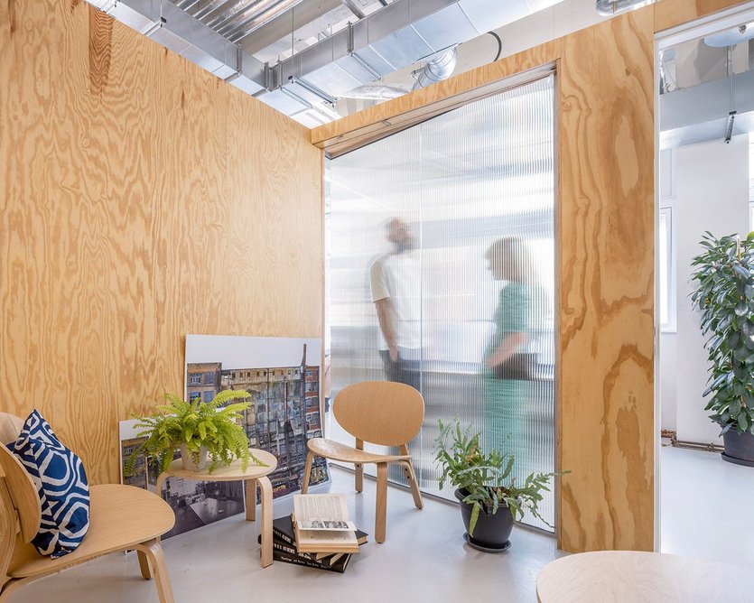 Freestanding plywood and glass pods offer privacy in the co‑working space.