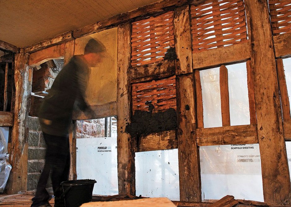 Wattle and daub being applied to new lath structure.