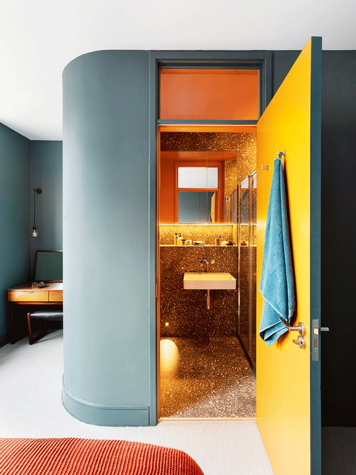 The bathroom makes neat use of the divided space of the master bedroom in the lower flat, with a warm blast of colour.