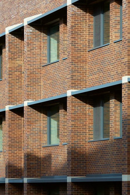 The brick fins of the deep-set facade are not structural but part of the solar shading strategy for classrooms. Triple glazed windows run along the insulation line.