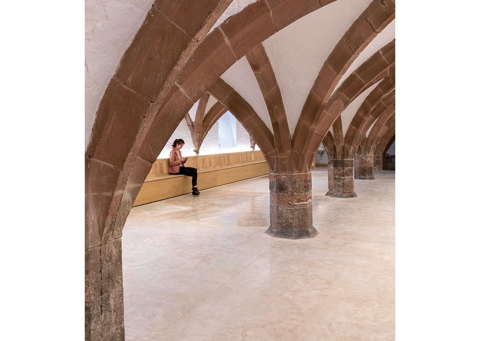The arches of the undercroft set off by a concrete floor with walls lined by benches.