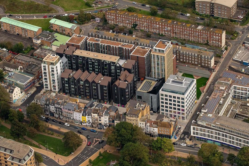 Aerial view from the south-east. The scheme sits 7m below adjacent housing on its western edge, with the massing of student accommodation clusters arranged to position taller elements away from the site boundary.