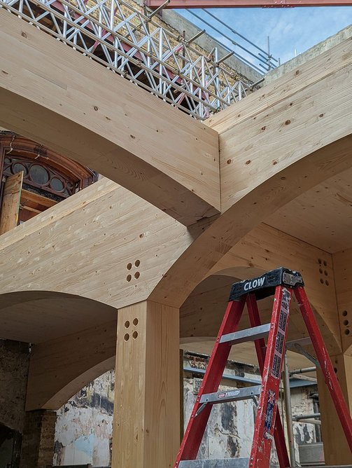 Longer-run glulam beams connect to column heads with steel flitch plates. Interstitial beams use SHERPA connections.