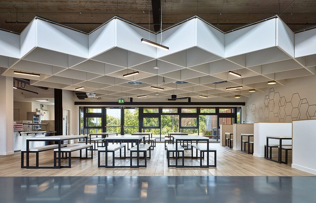 The dining area for secondary school pupils is on the ground floor with a ceiling grid of acoustic baffles. There are cross-plan horizontal view corridors to ensure clear lines of sight to the outside.