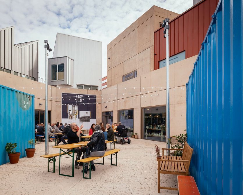The courtyard is contained and protected by the bright blue containers. Ground floor entry is in the corner where the building’s two arms meet.