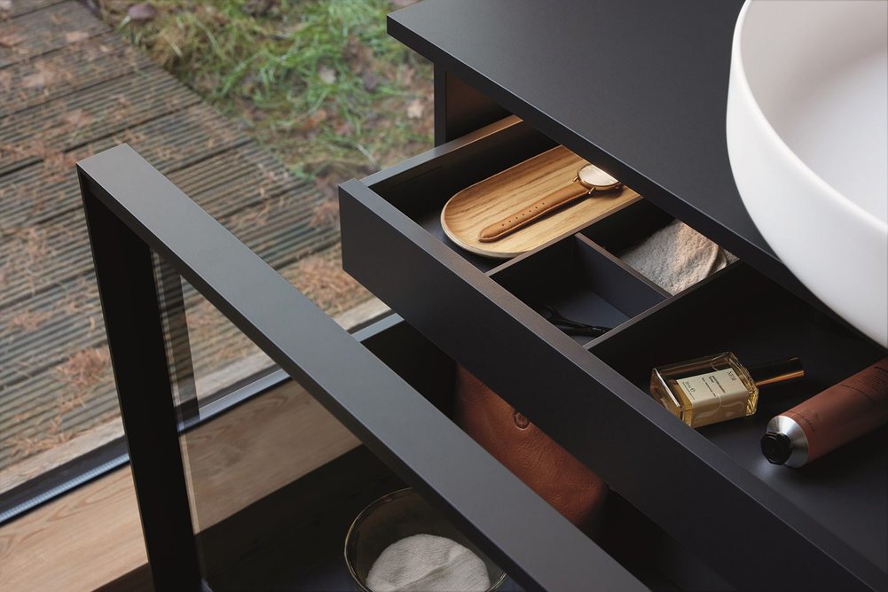 A horizontal handle integrated into the metal frame rounds off the pared-down furniture with a pull-out compartment.