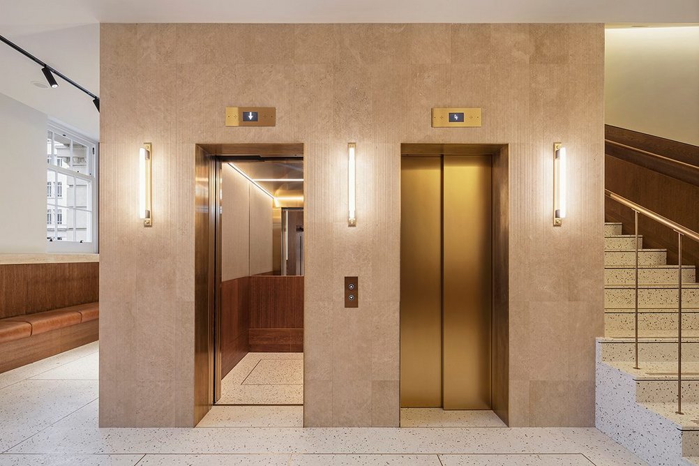 Vertical striations give the Italian travertine a more matt but no less luxurious quality. Elevator doors pick up on the brass theme.