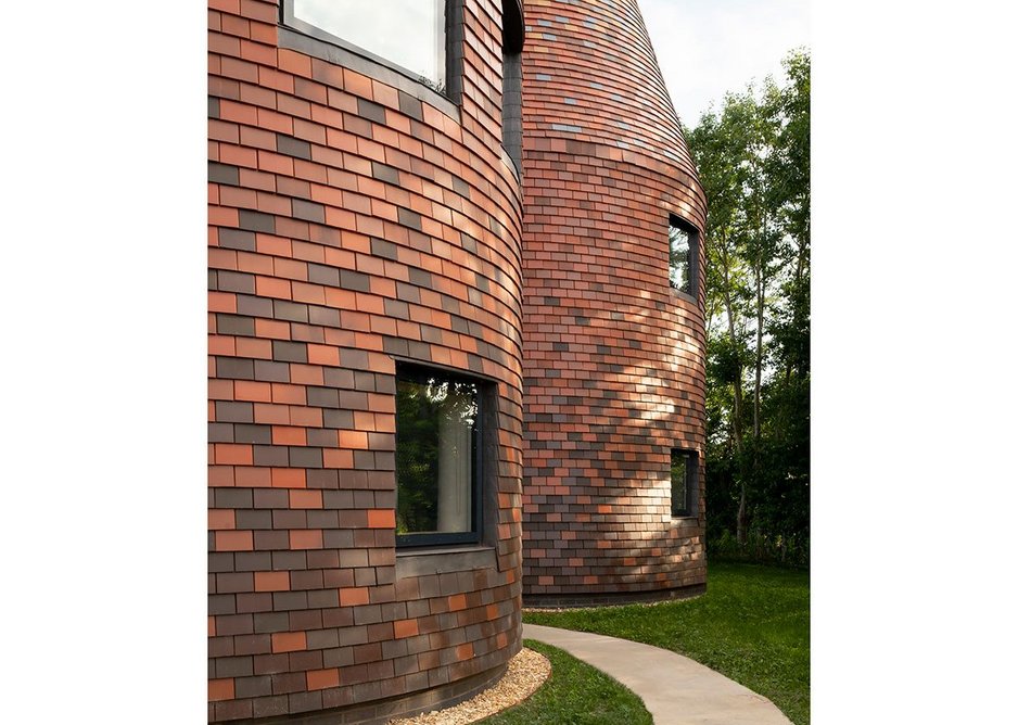 The house is entirely clad in ceramic tiles, changing from darker at the bottom to lighter at the top.