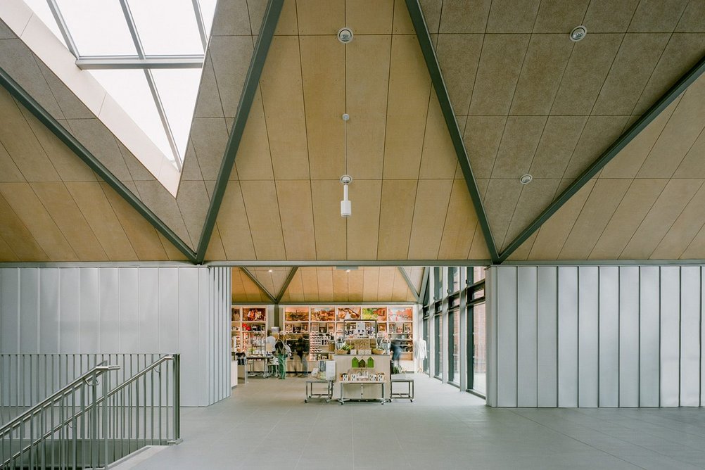 View through into the shop, showing the metal standing seam wall finish, minimalist joints of the rafters and the ceiling alternately infilled with ply and acoustic wood fibre insulation board.