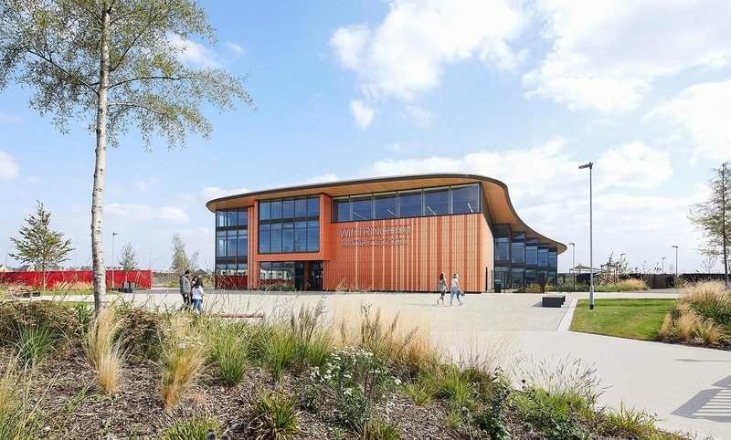 Clad in colourful terracotta, the school is positioned on the edge of what will be the new main square for Wintringham, an extension to the town of St Neots, Cambridgeshire.