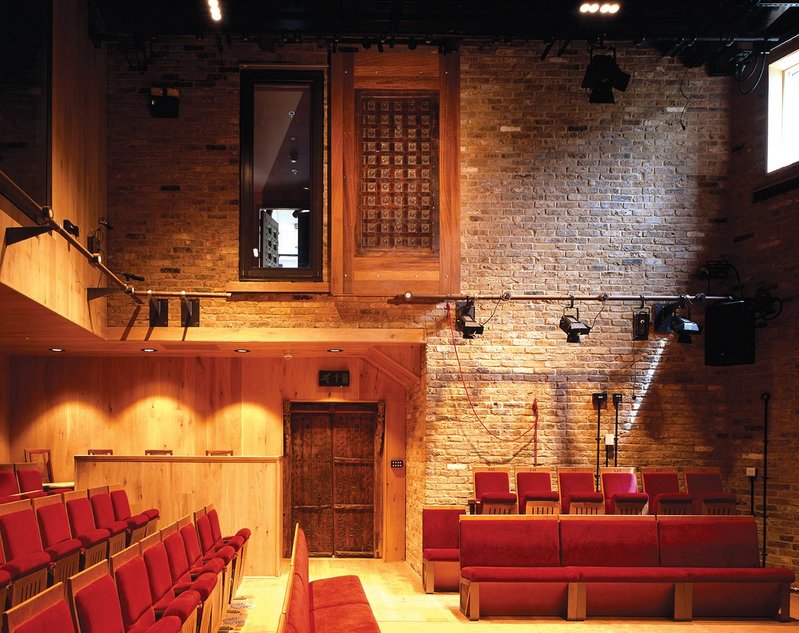 Visitors enter through ornate Indian double doors into an unexpected cosy theatre of exposed brick, oak panelling, red seats, natural light and a rammed earth stage.