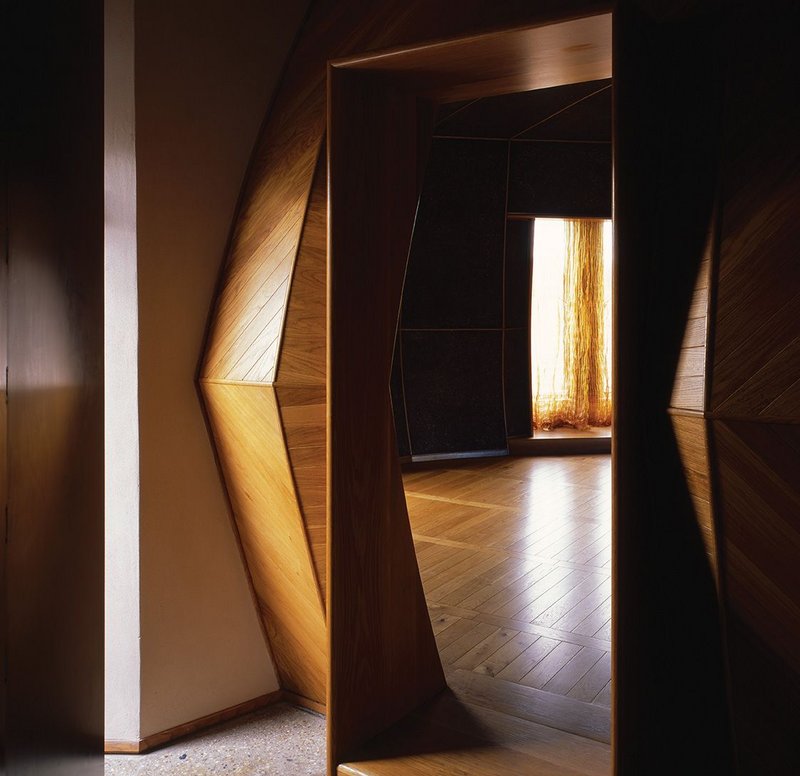 The threshold to House A’s yurt living space. The polygonal timber structure’s darkness is relieved only by glass oculi and amber light bleeding through the copper mesh curtain