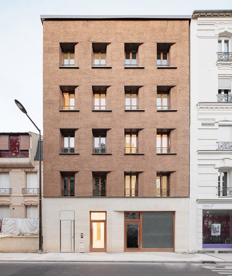 The building comprises four residential storeys faced in rammed-earth blocks above a shop with a stone facade.