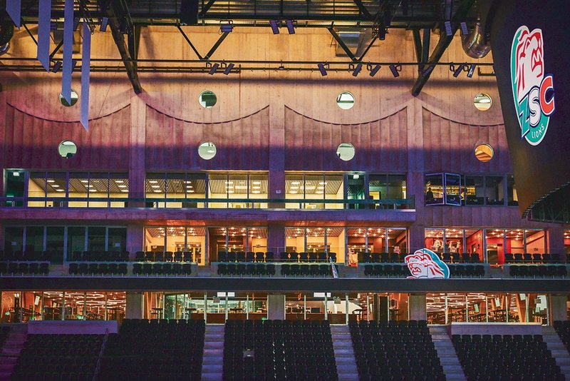 The arena’s internal north wall, lit dramatically, with restaurant below and corporate boxes, press and security above. Circular windows look down from club office and physio spaces.