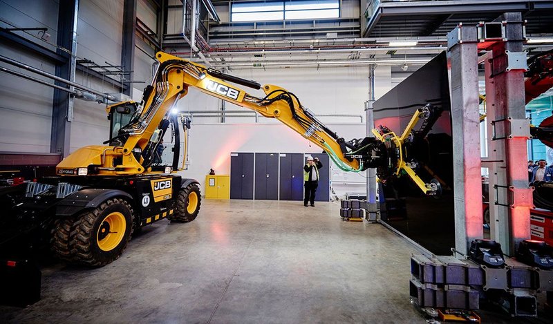 A JCB with a modified end effector places a panel into a frame, demonstrating a semi-automated technique that could be applied in construction