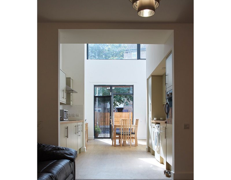 Inside a light-filled living space, the front door with galley kitchen at the centre.