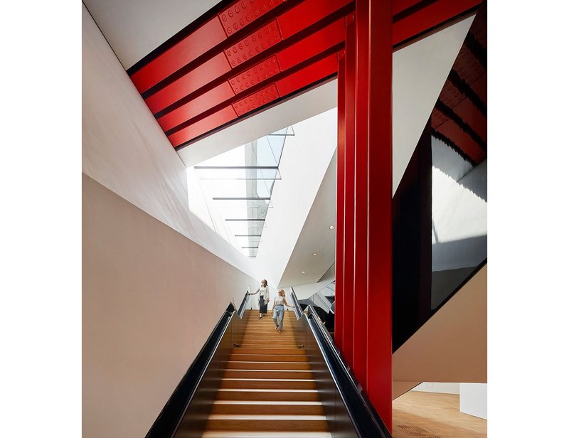 The staircase passes below exposed red-painted steels that are holding up the wall of the old museum above.