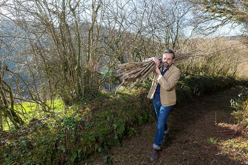 Niall Maxwell of Rural Office for Architecture at his farm near Carmarthen, shifting a bundle of hazel sticks.