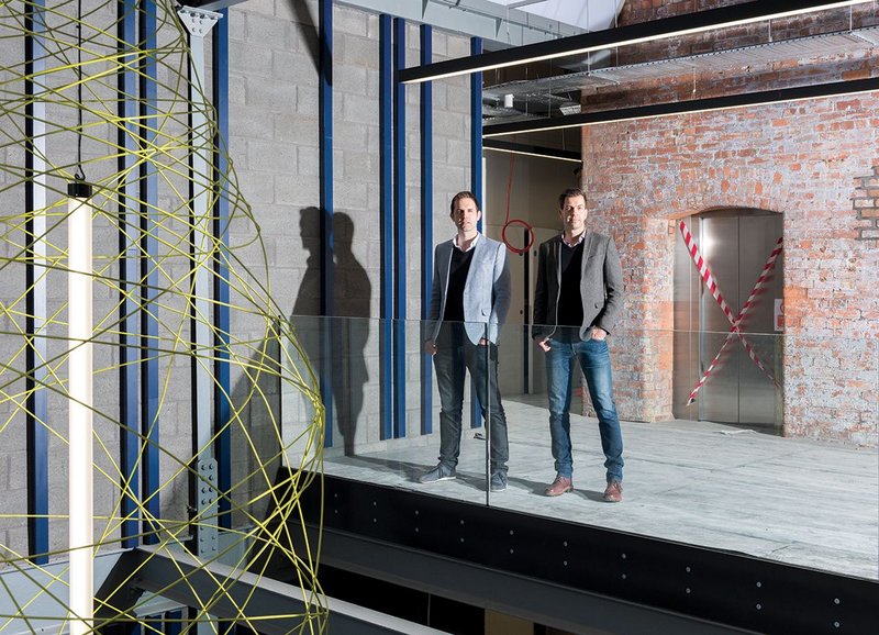 Nick Moss (left) and Andrew Edmunds on the atrium of their refurbishment project Stubbs Mills in New Islington, Manchester. The bobbin inspired lamp hangs to the left.