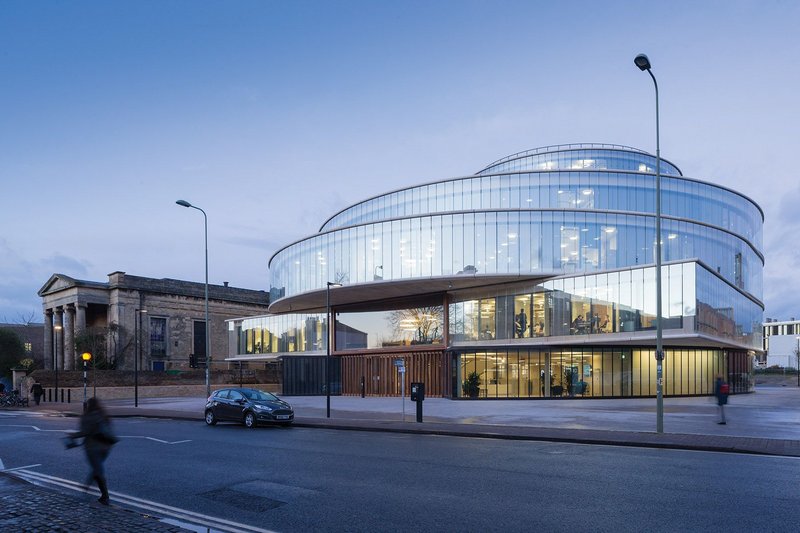 The Blavatnik School of Government viewed at dusk from the main facade onto Walton Street; partially reflecting, partially transparent, a building half dematerialised.