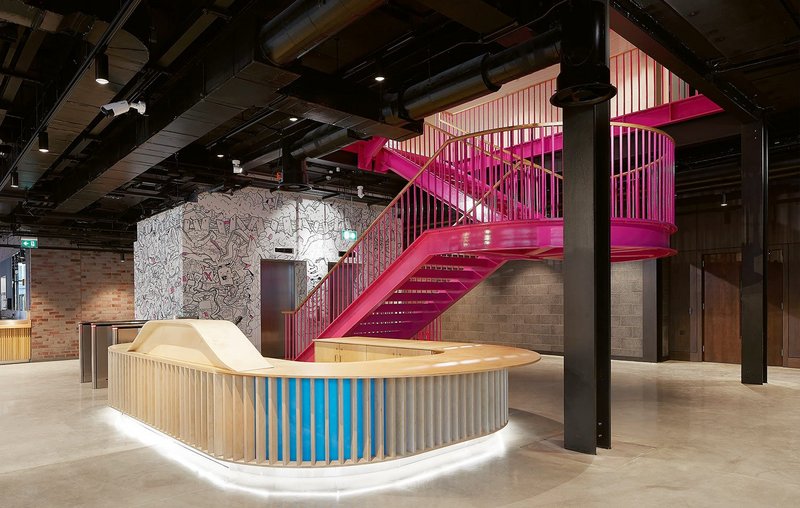 A bright pink staircase contrasts with the warehouse aesthetic of the ground-floor foyer.