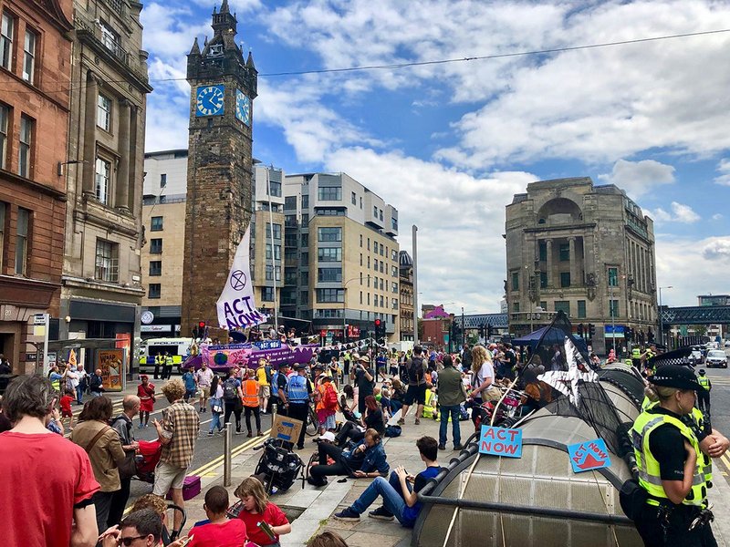 Example of civil disobedience: Glasgow’s Summer Uprising transformed the historic Trongate, carrying its message in both English and Scots Gaelic on the boat. For the Scottish and UK Governments to “Act Now”, to treat the Climate Emergency like the emergency it is: to halt biodiversity loss and reduce greenhouse gas emissions to net zero by 2025; and “The Future You Fear Is Already Here”: showing solidarity with climate refugees and those already suffering daily impacts of climate breakdown in the Global South and Indigenous North. July 2019.