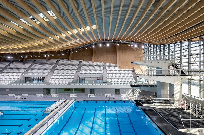 Inside the Paris Olympics Aquatics Centre looking north, showing diving boards and the flexible pool beneath a timber beam structure.