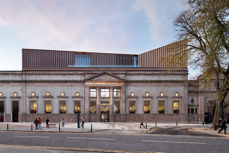 Granite entrance facade with new angled copper-clad rooftop extension.