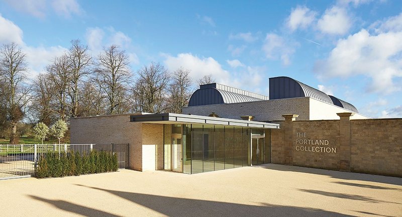 The new gallery is set behind the existing stone walls of a former indoor gallop, while the entrance pavilion extends in front.