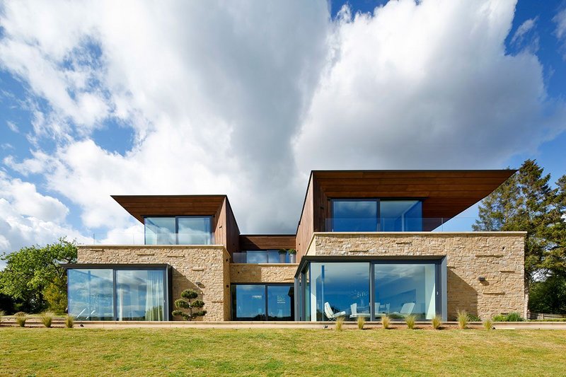 Expansive reflective glazing by Schüco fills the Surrey home with light while lessening the impact of the building in the landscape it occupies.