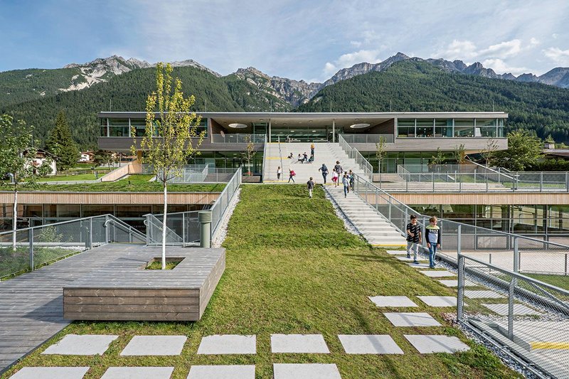 On the roofs of the school, one finds a terraced landscape with green lawns, incised courtyards, wooden slabs and staircases leading up the different levels.
