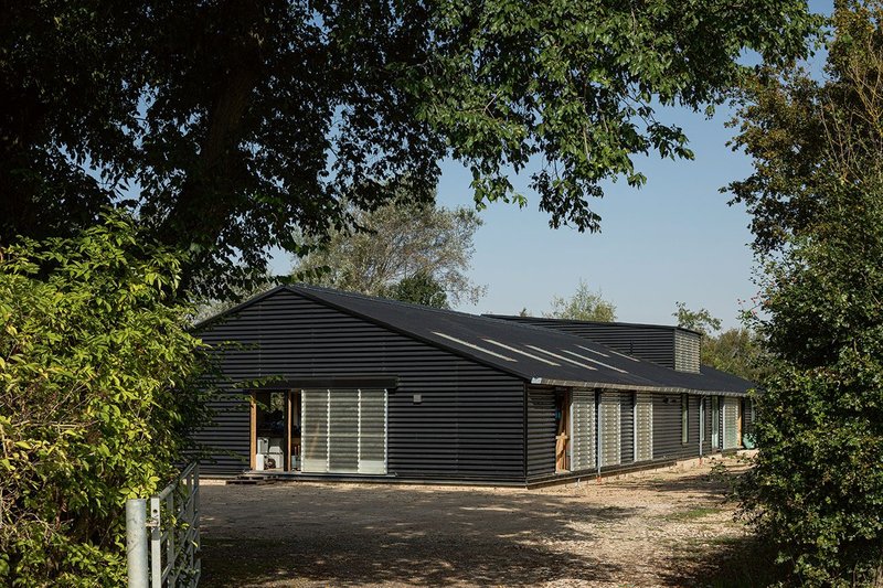 The building’s gable faces the road. Fibreglass rooflights and sliding doors enliven black cladding.