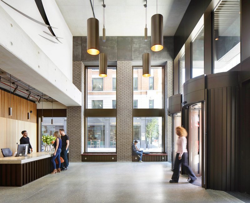 Double height main entrance, where brick piers and exposed concrete combine with timber panelling and feature lights