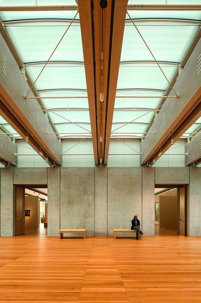 The dual glulam timber beams, spaced 3.5m apart, are spanned by subtle, curved, double-glazed panels and cross-braced. Lighting and sprinklers run discreetly between them.
