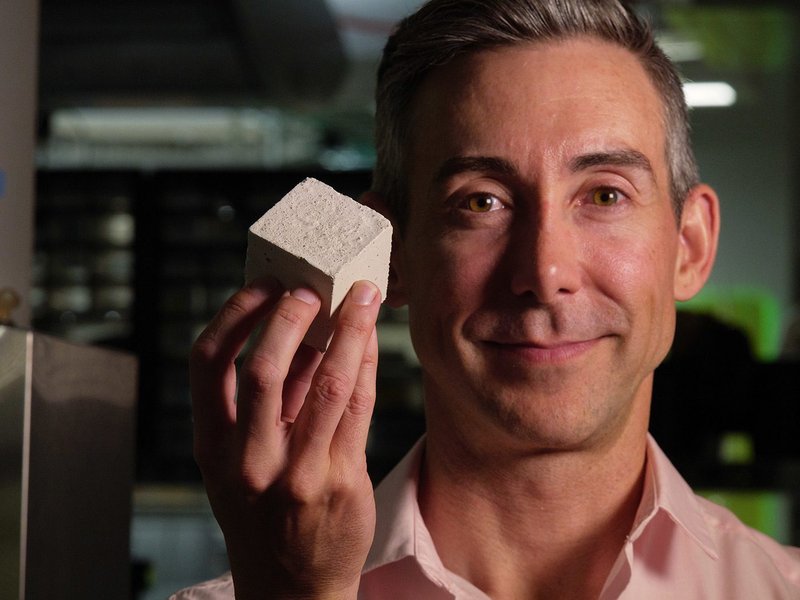 Wil Srubar, professor at the University of Colorado Boulder, holding a sample cube of concrete containing biogenic limestone produced by calcifying algae.